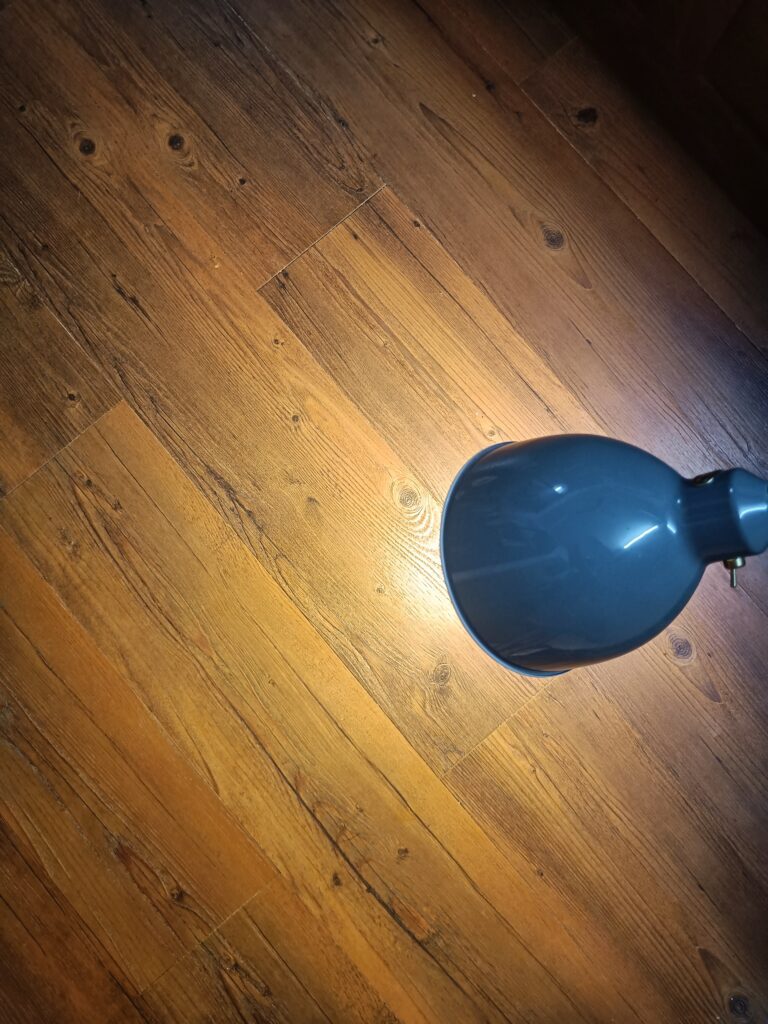 Blue desk lamp casting light onto a wooden floor.