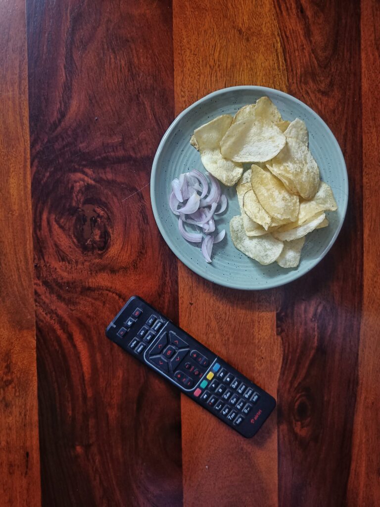 A plate of plain salted potato chips and sliced onions on a wooden table beside a television remote, the nightly ritual before The 50 began.